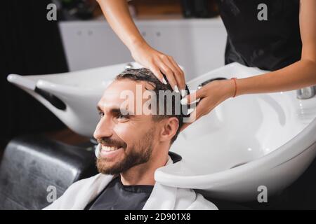 hairstylist washing hair of happy, bearded man in barbershop Stock Photo