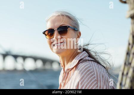 Beautiful mature woman in sunglasses looking at camera and smiling outdoors Stock Photo