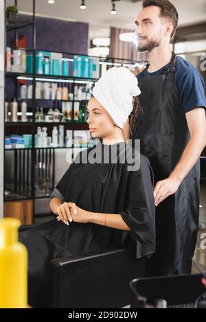 bearded barber standing behind woman with hair wrapped in towel Stock Photo