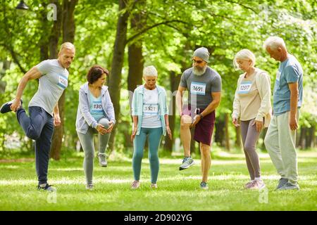 Group of senior men and women taking part in marathon training stretching legs just before running in park Stock Photo