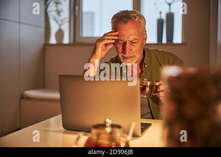 Senior man having a headache from working on laptop Stock Photo