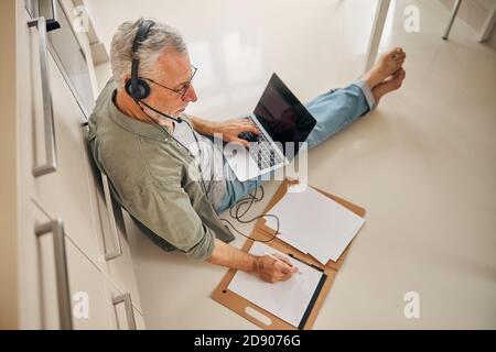 Focused senior gentleman sat on floor and working from home Stock Photo