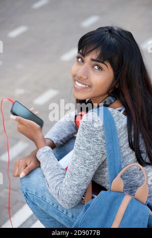 Portrait from behind of smiling Indian female student holding mobile phone Stock Photo