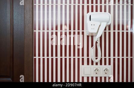 A white hair dryer hanging on tiled wall in a bathroom Stock Photo