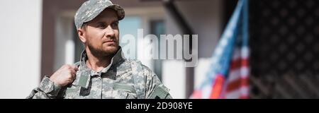 Military serviceman looking away with blurred american flag on background, banner Stock Photo