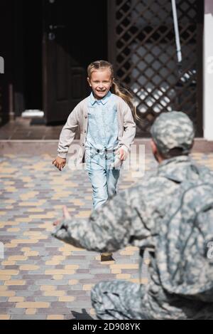 Happy girl running, with blurred father in military uniform on foreground Stock Photo
