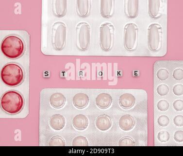 Concept of health, cardiology, heart disease. Words STROKE on white cubes, tablets in blisters on a pink background. Flat lay. Stock Photo