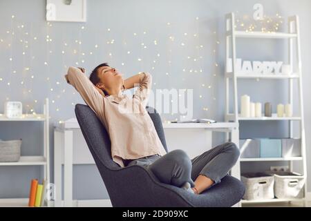 Relaxed young woman leaning back in armchair in home office happy that the work is done Stock Photo