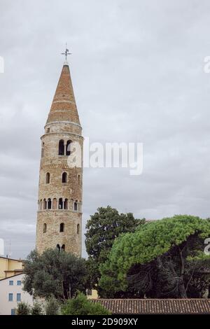 Round, medieval bell tower immersed in the clouds in Caorle, Italy, with trees Stock Photo