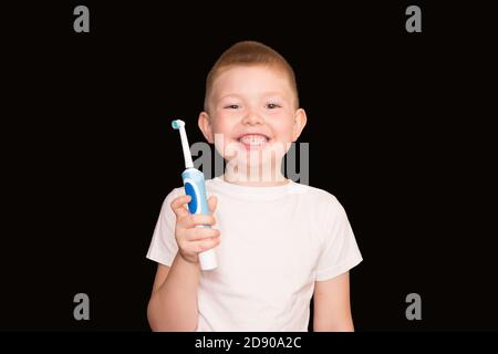 A boy brushes his teeth with an electric toothbrush on a black background. Stock Photo