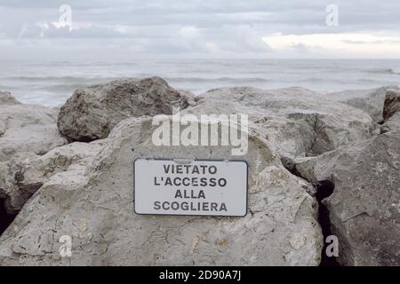 Rainy sky with a lot of clouds on a rocky beach, with a sign that forbids access to the cliff Stock Photo