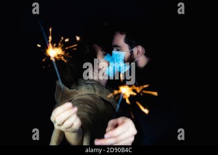 Young couple wearing protective face masks for Coronavirus and holding sparklers for New year's eve, 2021 and Covid-19 concept Stock Photo