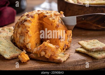 Closeup of a sliced cheddar cheese ball and crackers on a rustic cutting board Stock Photo
