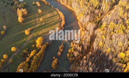 Aerial view from drone of curve mountain river, fall bald forest, green meadow and empty country ground road. Beautiful autumn nature landscape on sun Stock Photo