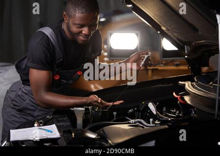 professional car mechanic is examining engine under the hood at auto repair shop, make notes, checking notes in notebook Stock Photo