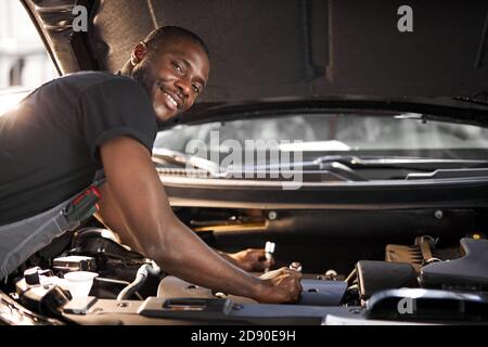 handsome guy repairing auto's hood, using tools. wearing unifrom, concentrated on work Stock Photo