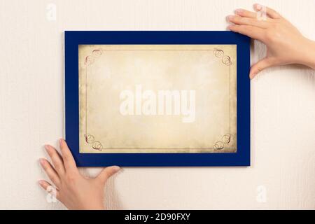 mockup diploma. woman hanging photo frame mockup on wall. OLD grunge certificate with vintage ornamental frame mockup Stock Photo