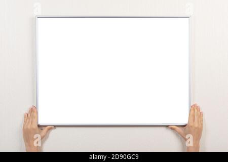 woman hands hold silver blank frame. mockup frames for picture of certificate, diploma or photo. woman hanging photo frame mockup on gray wall Stock Photo