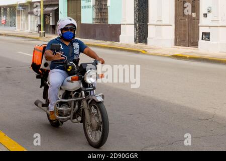 Motorcyclist wearing a face mask because of the ongoing pandemic doing food delivery in Merida Mexico Stock Photo