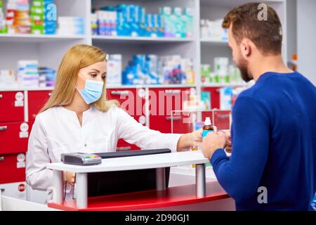 young professional druggist give medications to customer in modern drugstore, consult and recommend, wearing medical mask protecting from coronavirus covid-19 Stock Photo