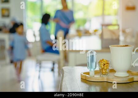 Mini portable alcohol gel bottle to kill Corona Virus(Covid-19) and biscuits and coffee cup on table with blurred image of a family eating at restaura Stock Photo