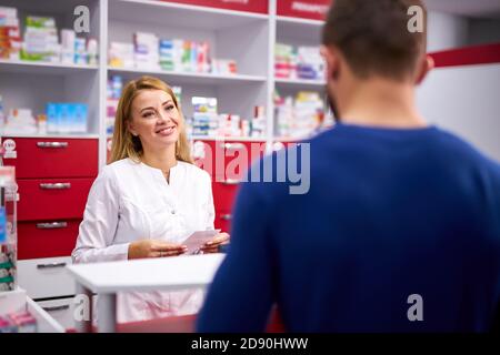 young caucasian helpful female druggist dealing with a male customer, explaining a prescription to ill patient, client