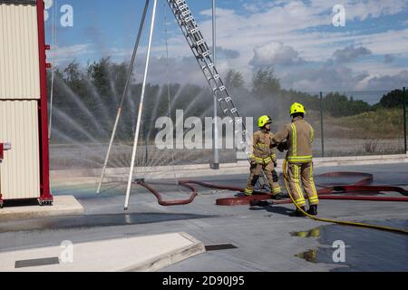 Two English firefighters in full protective equipment checking the function of a fire hose at Ossett fire station in Wakefield West Yorkshire England Stock Photo