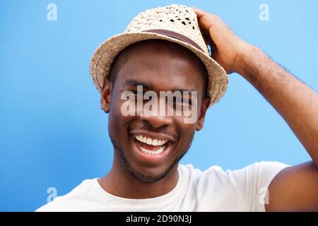 Close up portrait of cool young black guy with hat smiling against blue background Stock Photo