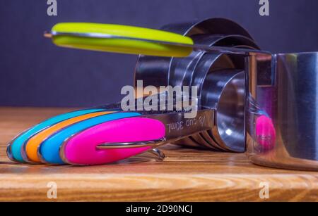 Closeup POV shot of a set of different sized, stainless steel measuring cups, with colour coded handles, on a pine kitchen work surface. Stock Photo