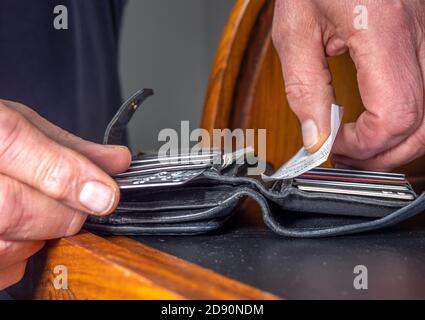 Closeup POV shot of a man’s hands putting a shopping receipt into an open leather purse / wallet, alongside various credit cards. Stock Photo