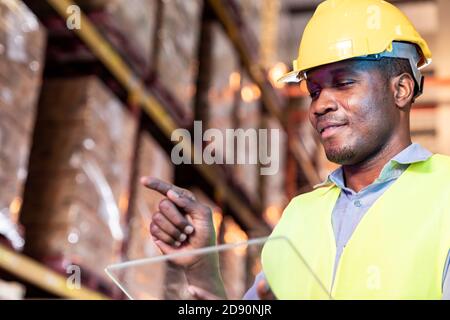 Portrait of african black warehouse worker hold tablet and touch on virtual screen in front of him in large warehouse distribution environment. Using Stock Photo