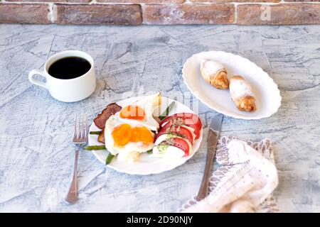 Italian breakfast with coffee and caprese. Fried eggs with bacon, tomatoes, Mozzarella, green beans and croissants. Delicious breakfast served on table with napkin. Soft focus Stock Photo