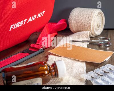 Close POV shot of a first aid kit box, with various items on a table – bandage, scissors, sticking plasters and a bottle of ointment. Stock Photo