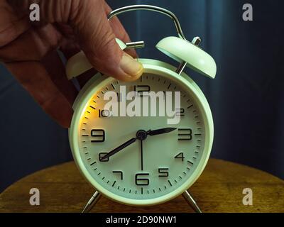 Closeup POV shot of a man’s hand pressing on the back of a traditional alarm clock and activating a glowing light to see the time. Stock Photo