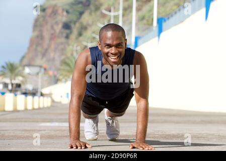 Portrait of happy young black man doing pushups outdoors Stock Photo