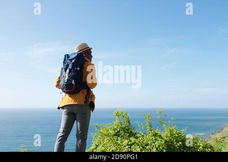 Portrait from behind of happy black man with backpack looking at sea view Stock Photo