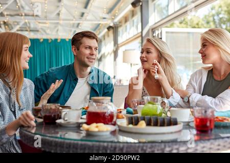 happy young caucasian friends gathering in cafe, sitting at table, chatting, talking.they are spending funny time, students or best friends meeting Stock Photo