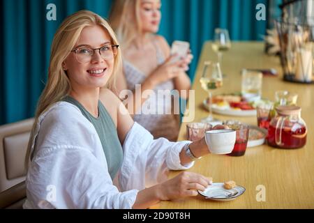 cheerful caucasian woman drinking coffee in cafe, young female sits at table with cup of coffee, look at camera and smile Stock Photo