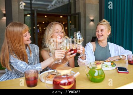 group of young friends clinking glasses with beverages in cafe, they share news, rest after work or celebrate something Stock Photo