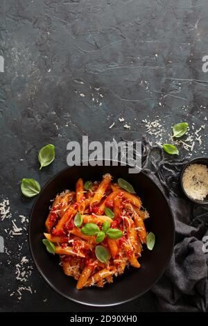 Penne pasta with tomato sauce, parmesan cheese and basil on dark background. Top view with copy space. Stock Photo