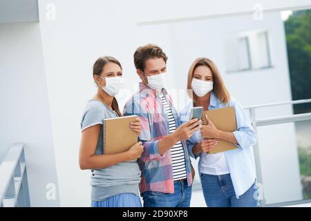 Couple of students wearing masks and using smartphone in the campus Stock Photo
