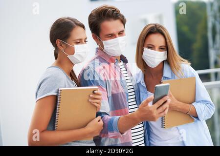 Couple of students wearing masks and using smartphone in the campus Stock Photo