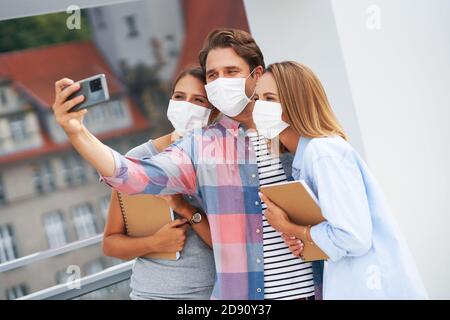 Couple of students wearing masks while taking selfie in the campus Stock Photo