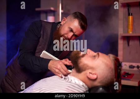 caucasian hipster client man visiting in barber shop shaving beard by professional hairdresser, stylish and and modern beard in salon Stock Photo