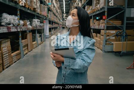 Asian business working woman wear mask using digital tablet checking stock of products in warehouse Stock Photo