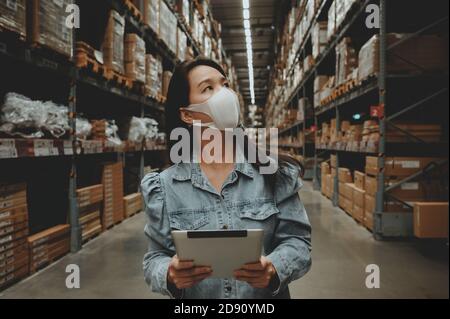 Asian business working woman wear mask using digital tablet checking stock of products in warehouse Stock Photo