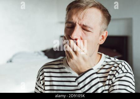 Young man feeling sore and tired. Frustrated millennial yawning in home office dressed casually having headache, sleep problem.  Exhausted after overw Stock Photo