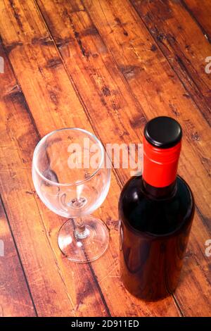 Bottle of red wine and an empty wine glass sat on old rustic floor boards Stock Photo