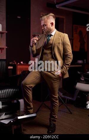 good-looking male in suit drinking alcohol, he holds glass of beverage in hands, posing alone Stock Photo