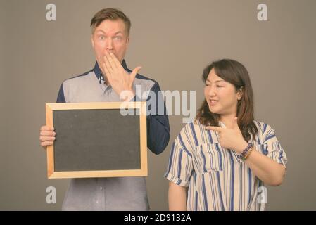 Young handsome businessman and mature Asian businesswoman against gray background Stock Photo